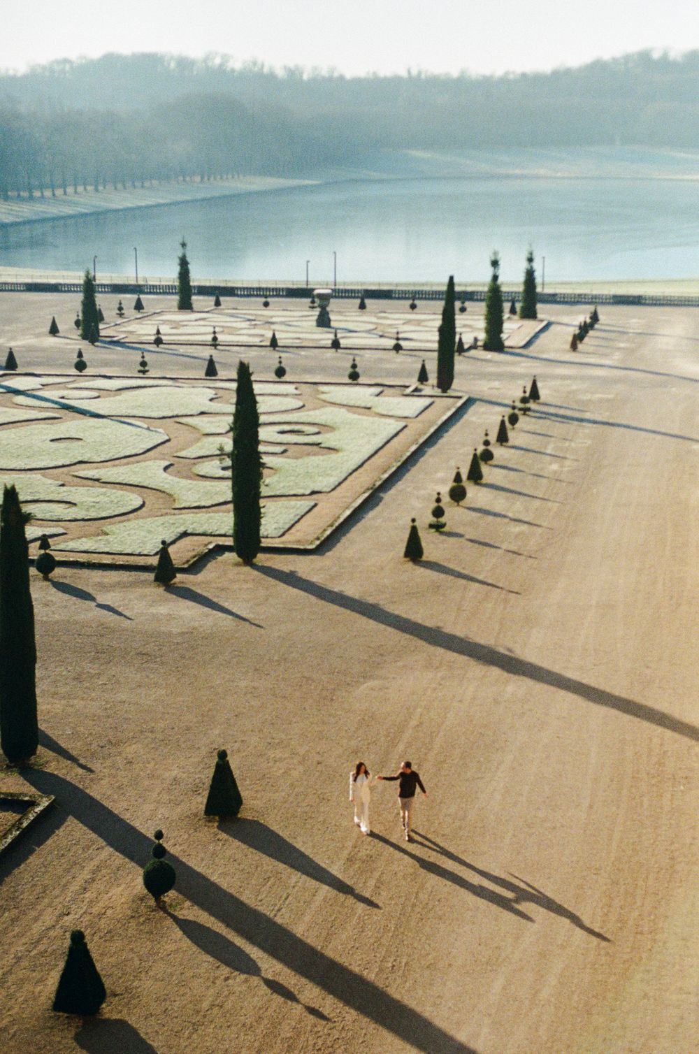 Long shadows stretch across a geometric garden with cypress trees and ornate pathways at sunset. 35mm paris film photographer