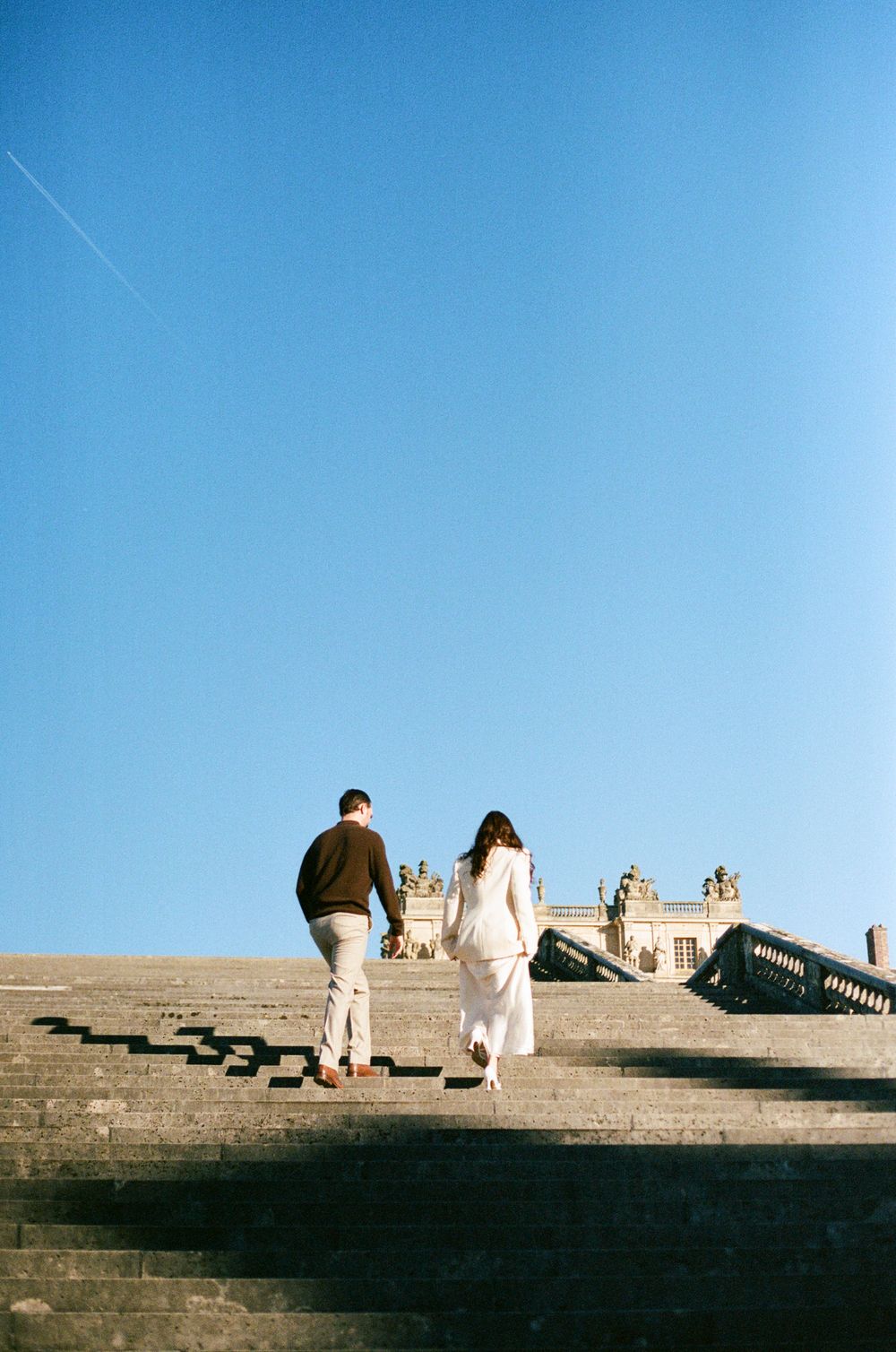 People sit and relax on stone steps against a bright blue sky at a historic monument.