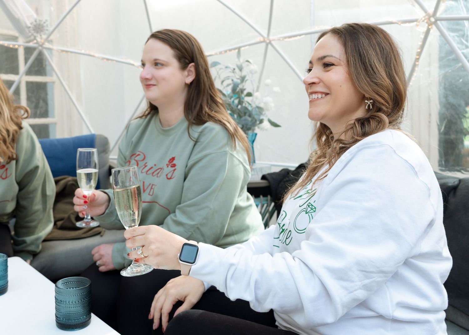 Bride surrounded by bridesmaids wearing matching sweatshirts — candid wedding celebration portrait