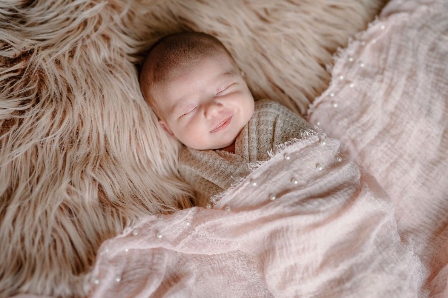 A newborn baby wrapped in a pink swaddle blanket lies on a pastel-colored knitted blanket.