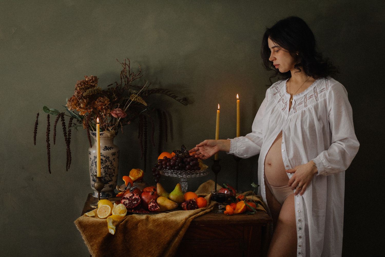 A moody fine art portrait series featuring a white nightgown against dark backgrounds with candles and flowers.