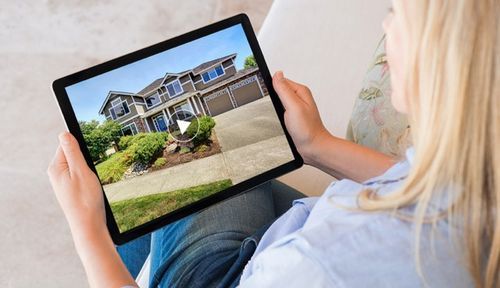 Person holding digital tablet showing different real estate property listings and exterior home photos.