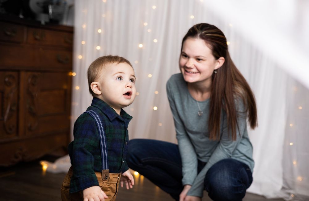 A mother and a child interact while standing in front of a wall with string lights.