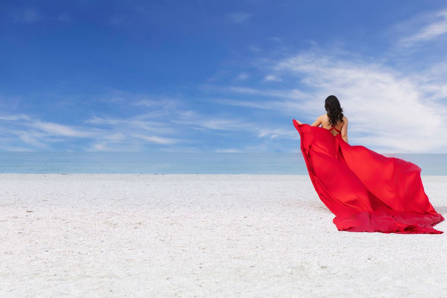 A flowing red fabric billows gracefully across a stark white salt flat landscape under bright blue skies.