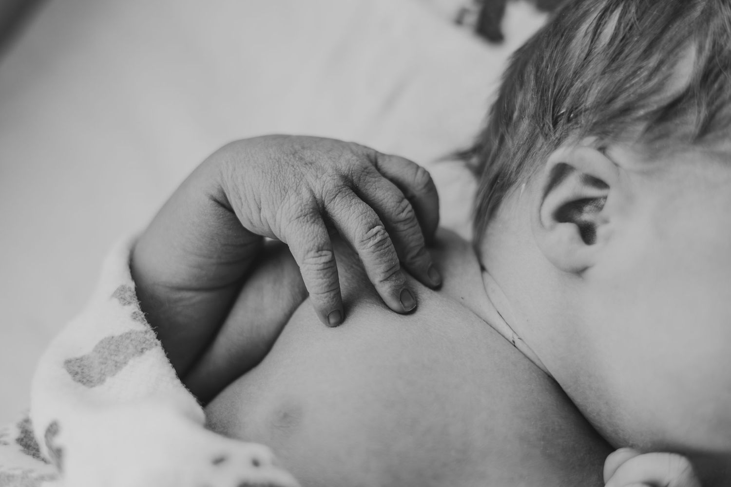 Black and white close-up of a newborn baby sleeping peacefully, with a tiny hand resting on their shoulder | Fresh 48 Hour Photos