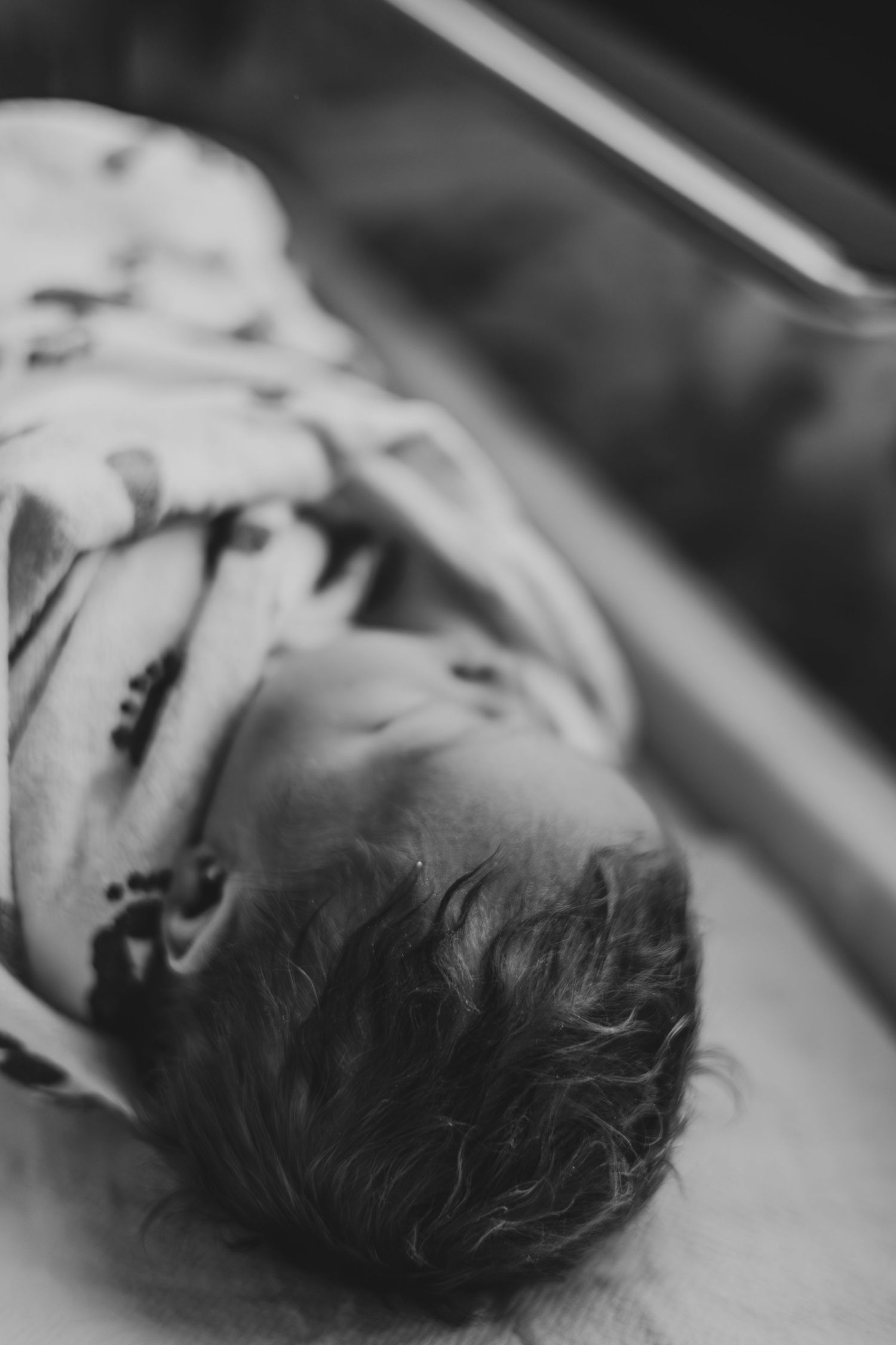Black and white photo of a newborn baby lying down, wrapped in a patterned blanket, with soft focus background | Fresh 48 Hour Photos