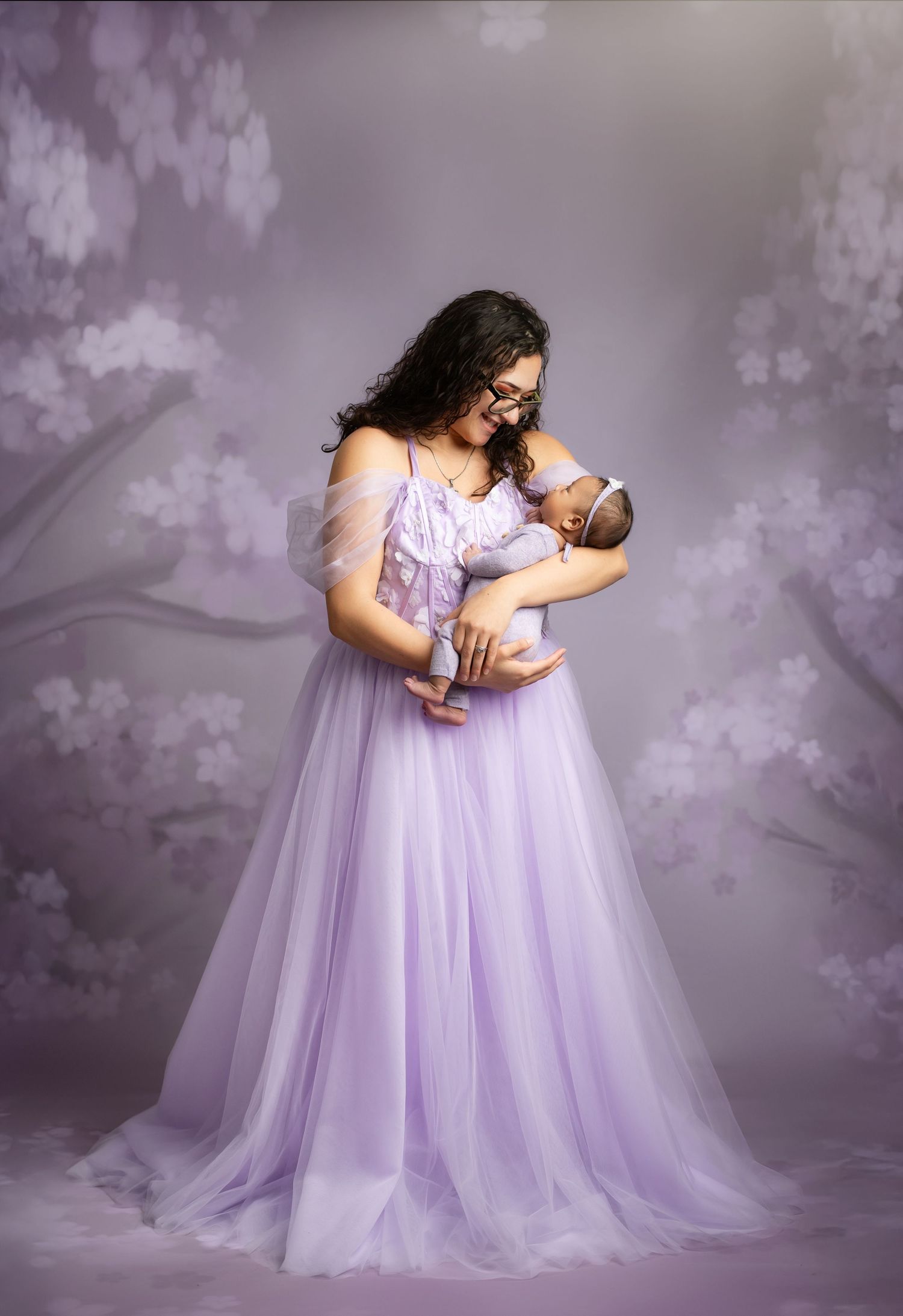 A tender moment captured in a dreamy purple setting with a flowing lavender tulle gown and newborn baby.