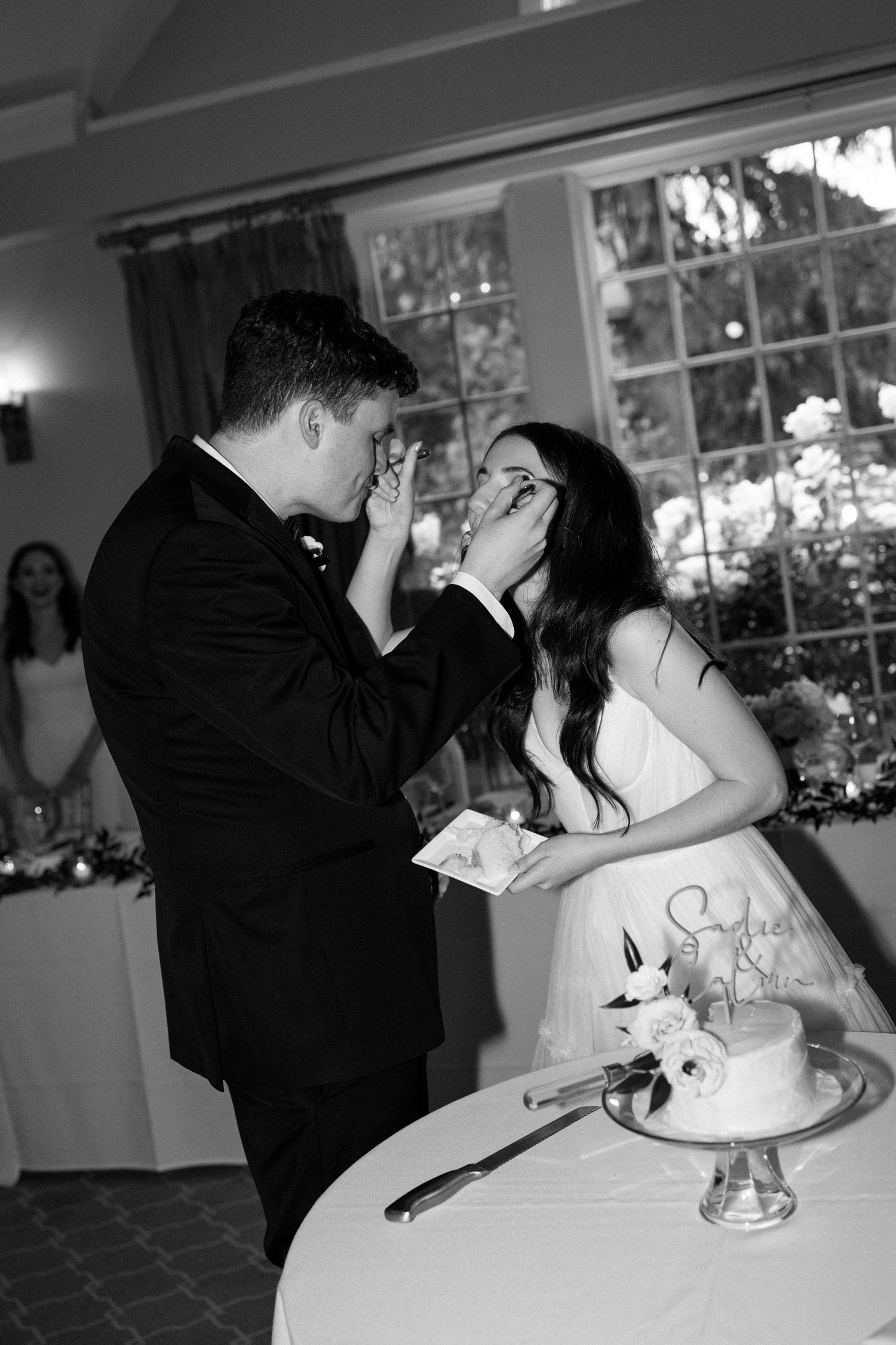 A romantic black and white photo series of a couple cutting their wedding cake and sharing a kiss at their reception.