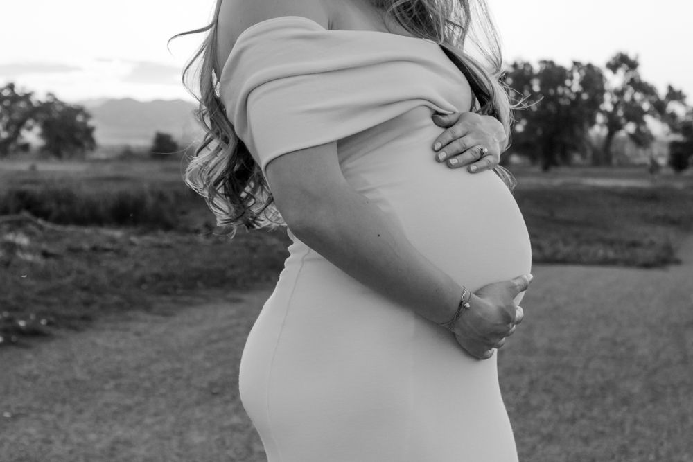 maternity photo of pregnant woman in off-shoulder dress cradling baby bump outdoors |Motherhood + Maternity Photographer in Westminster, CO