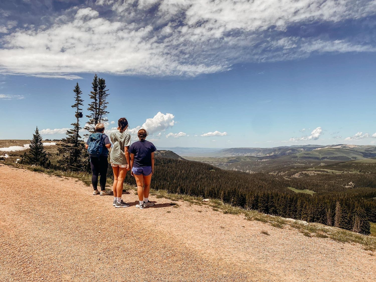Three hikers enjoying panoramic mountain valley views from a scenic overlook trail in Colorado.