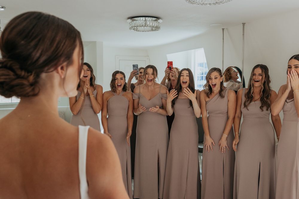 A row of bridesmaids in matching blush pink dresses show joy when seeing the bride for the first time at Lake Oak Meadows in Temecula.