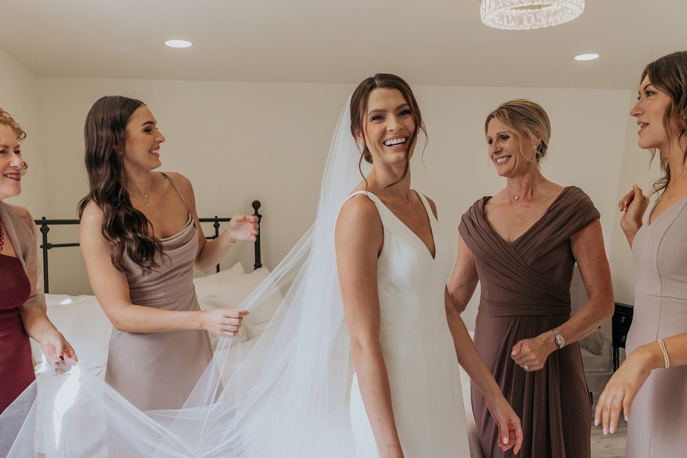 Bridesmaids in blush pink dresses help the bride get ready for her wedding day in a bright indoor setting at Lake Oak Meadows in Temecula.