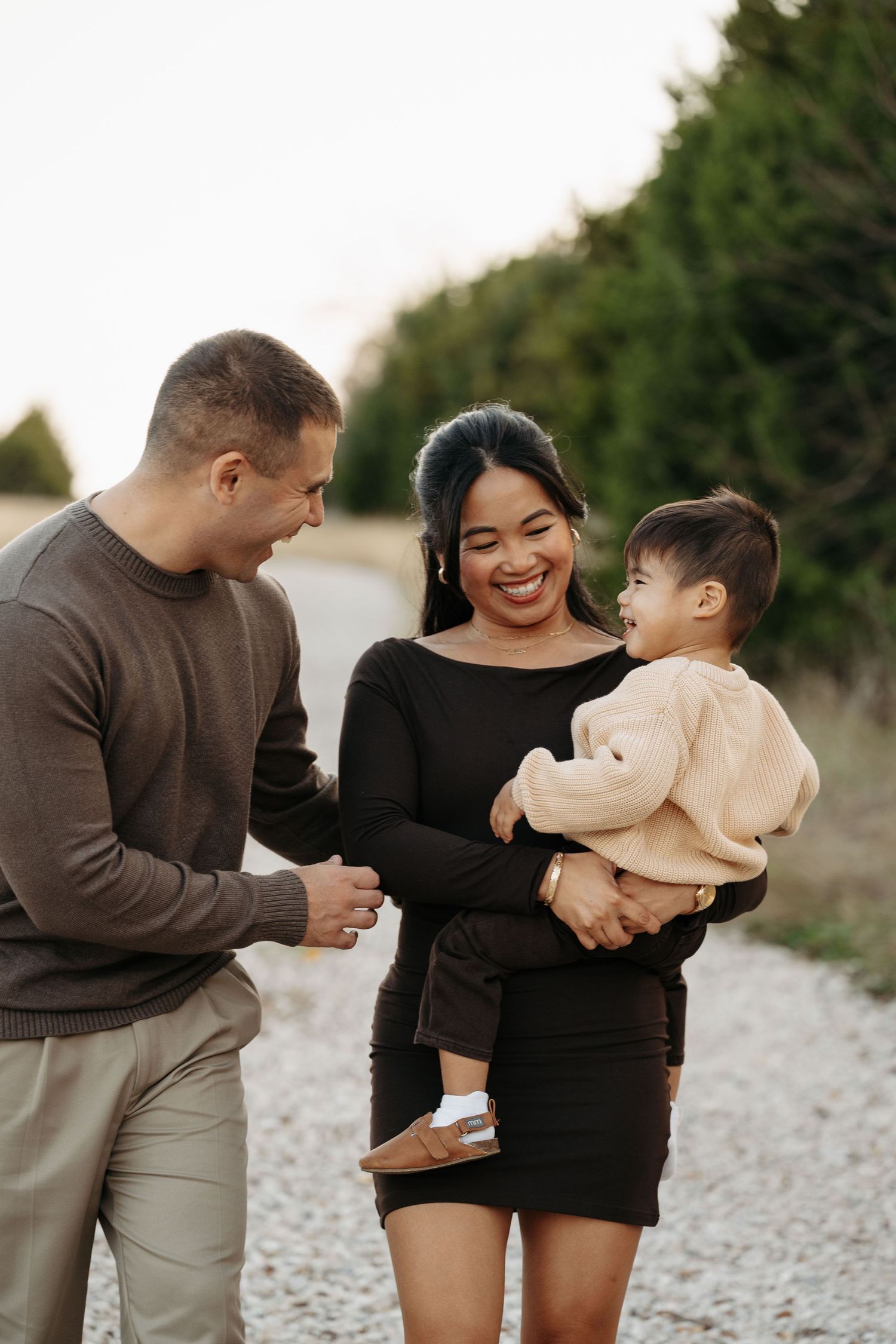 A family stands together in a grassy field at sunset wearing coordinated casual outfits in earth tones.