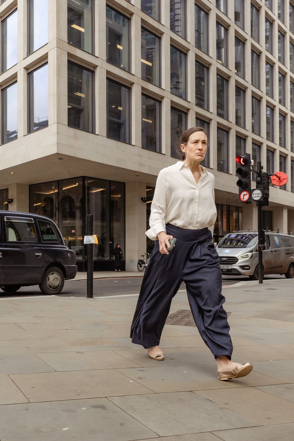 A sequence showing someone walking on a city sidewalk wearing wide-leg pants and a white shirt near office buildings.