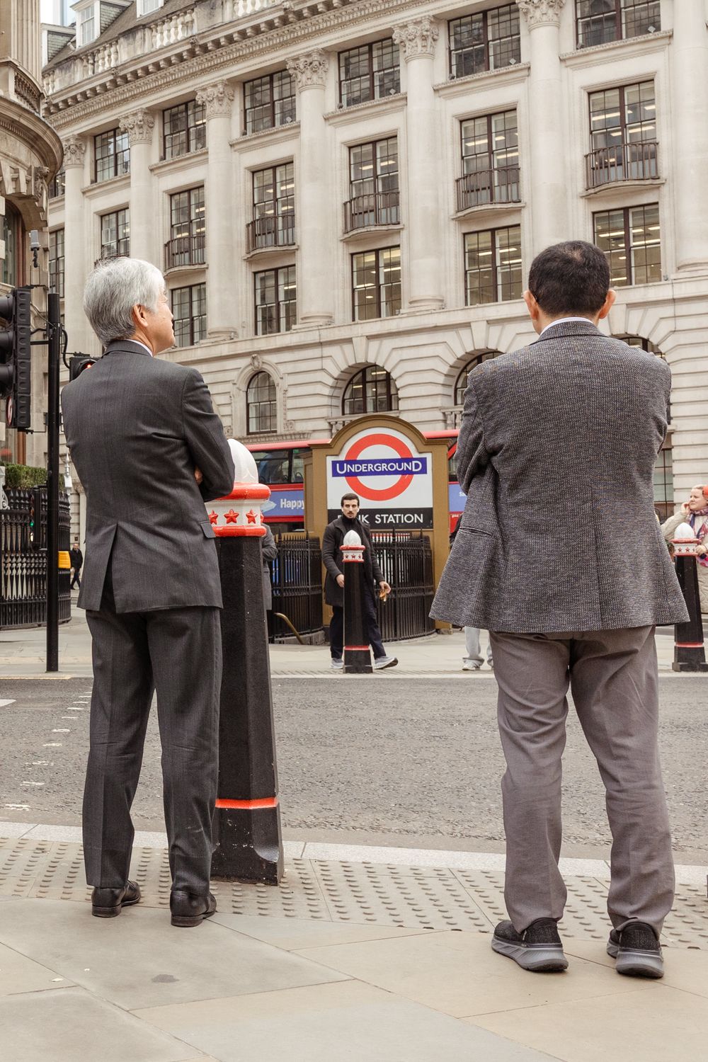 A series of photos showing two people in suits standing and looking at something in front of a classical building facade.