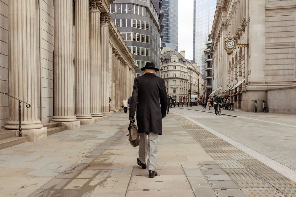 Person in dark coat walking along ornate colonnade in London's financial district.