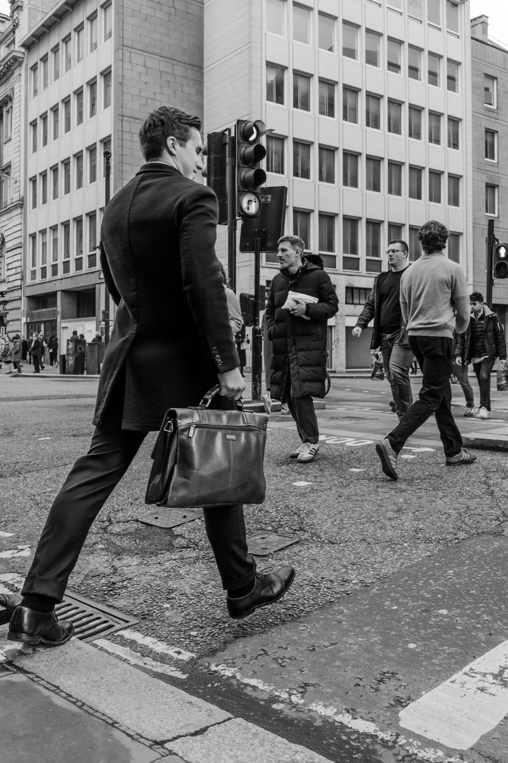 Black and white photos showing people crossing a city street with scattered leaves on the ground.