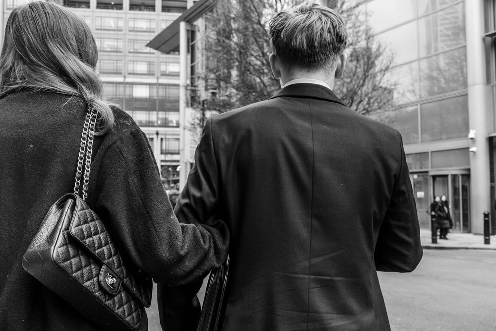 Black and white photo of two people in dark coats walking together on a city street.