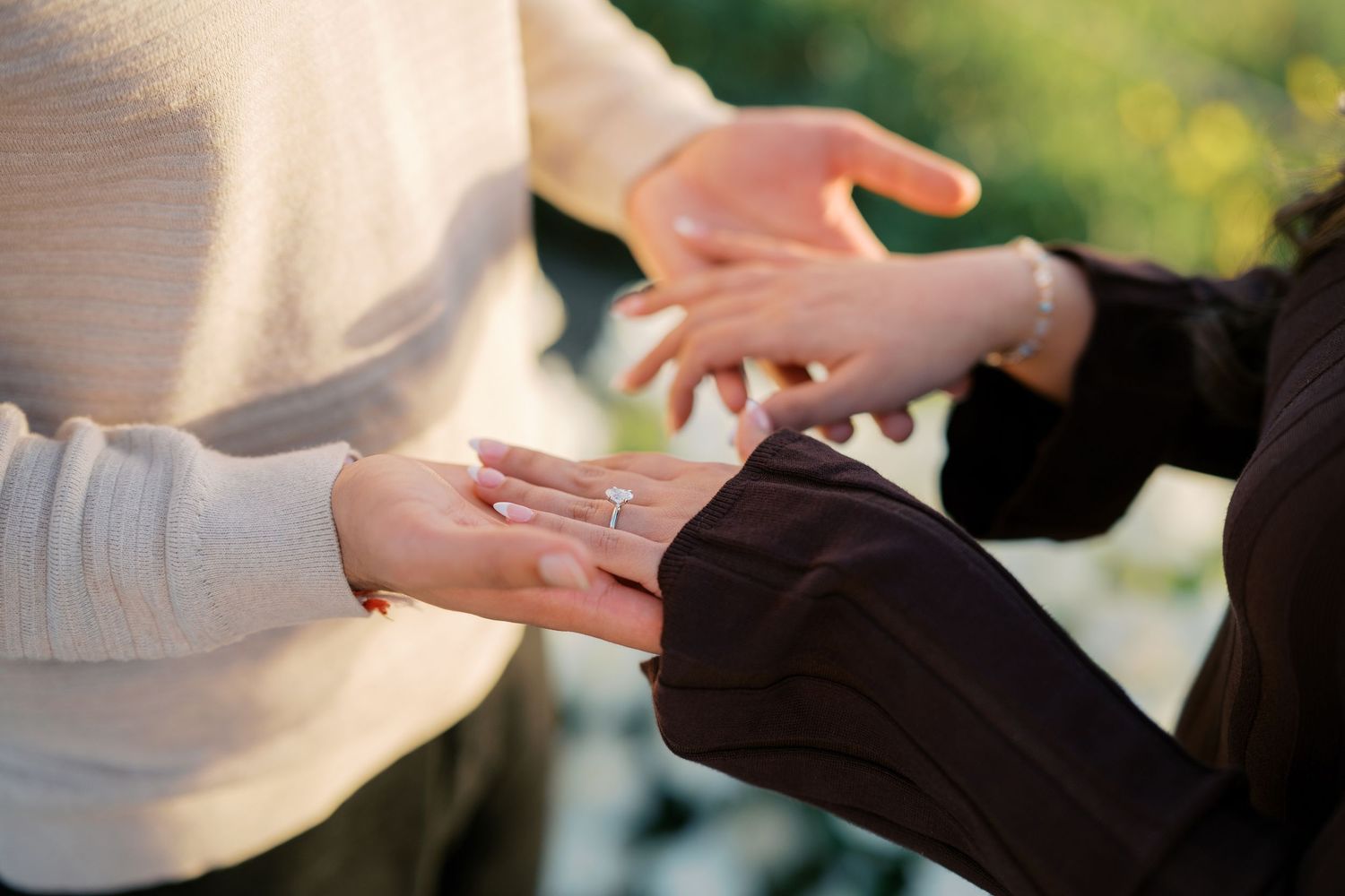 Close-up of hands exchanging something during a sunny outdoor moment while wearing knit sweaters.
