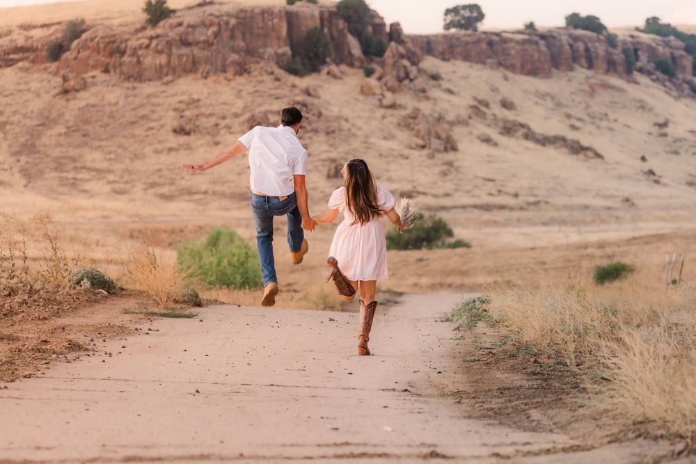 Couple walking along a desert trail with mountains in the background during golden hour.