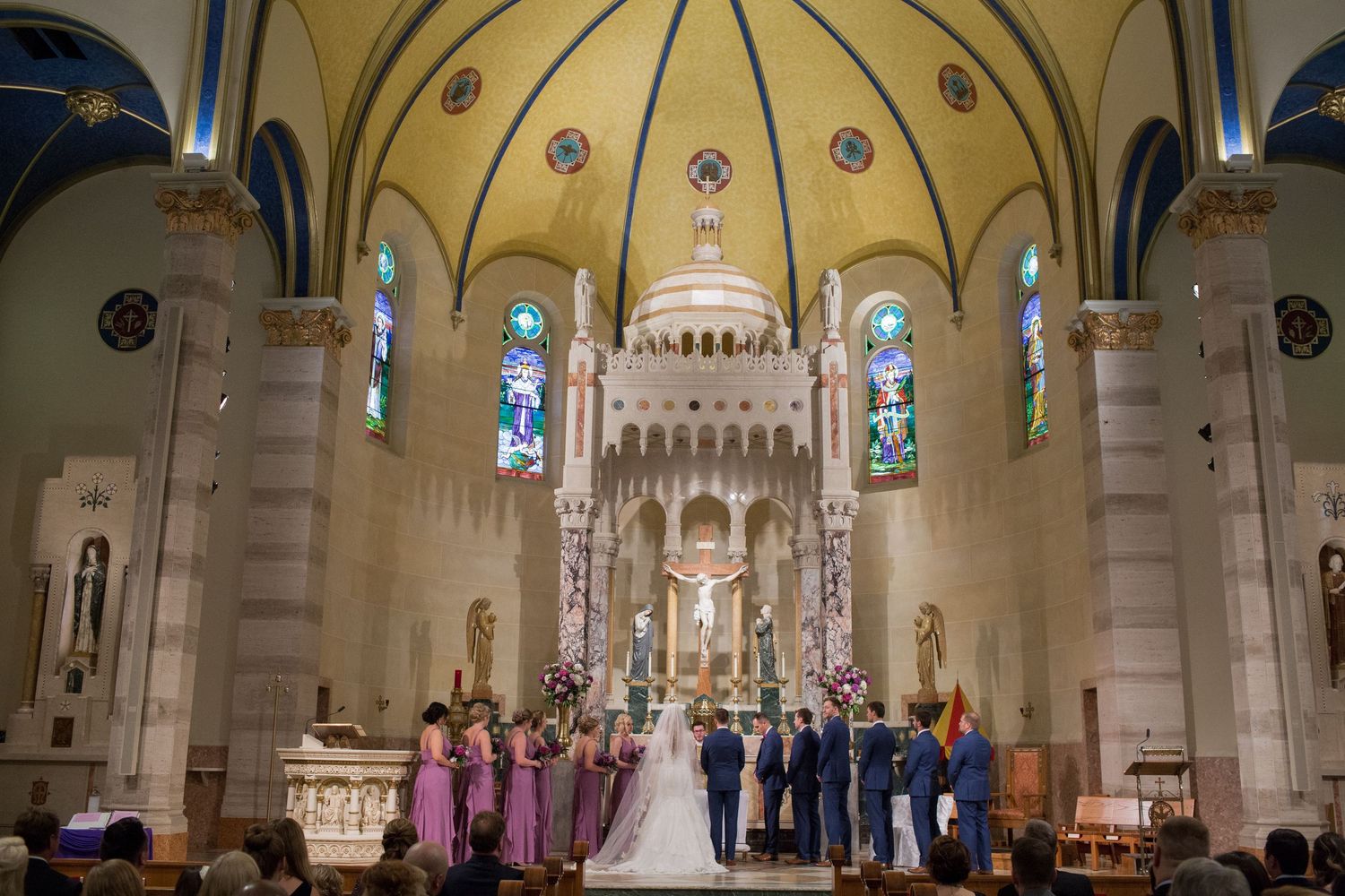 Wedding ceremony in a grand cathedral with yellow domed ceiling and stained glass windows.