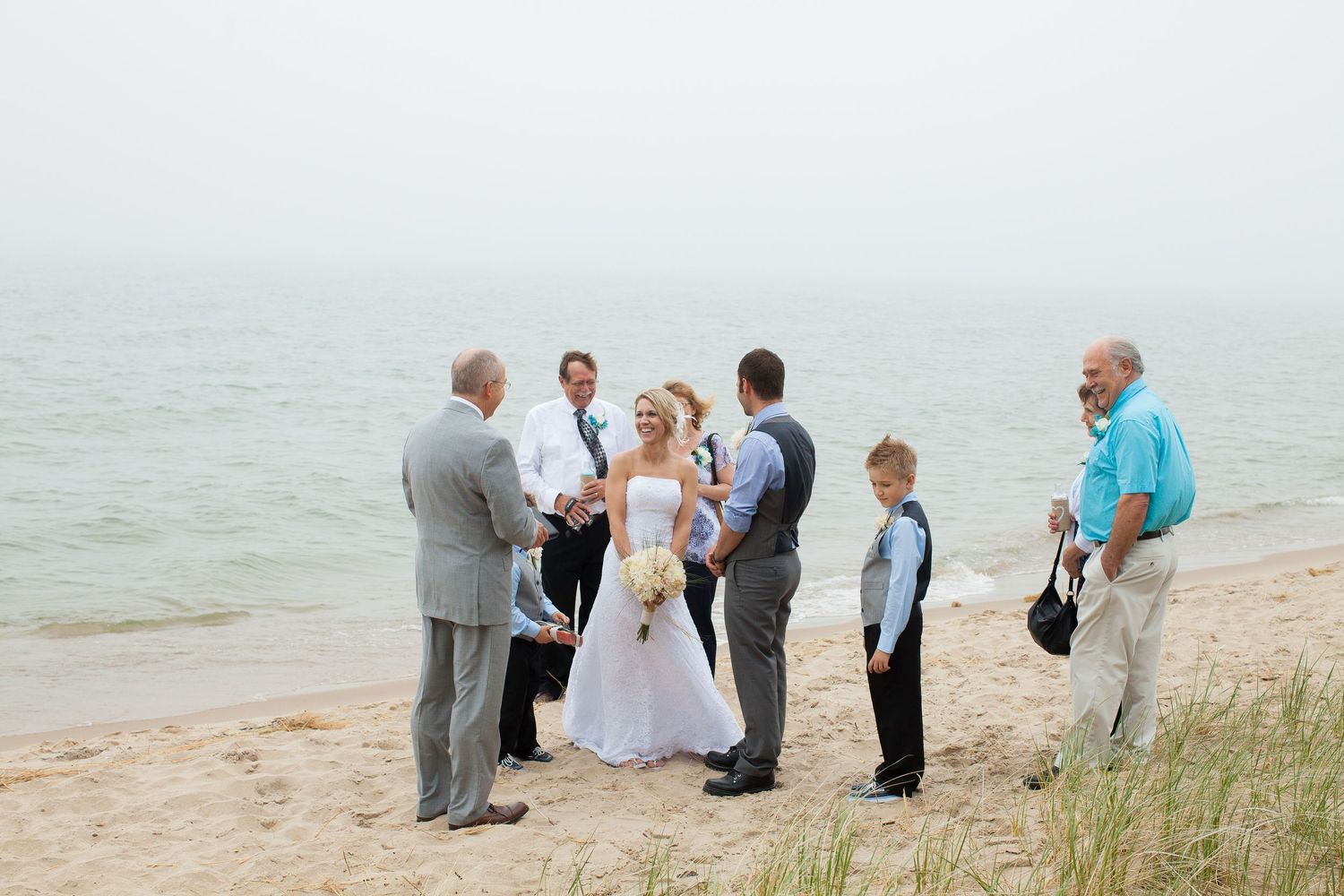 Wedding party gathered on a scenic beach with ocean views and natural dune grass in the background.