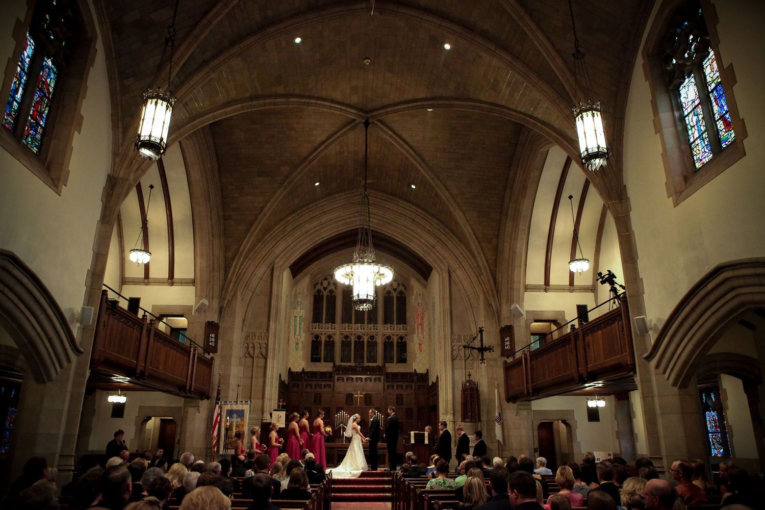Wedding ceremony in a historic church with vaulted ceilings and hanging lanterns.