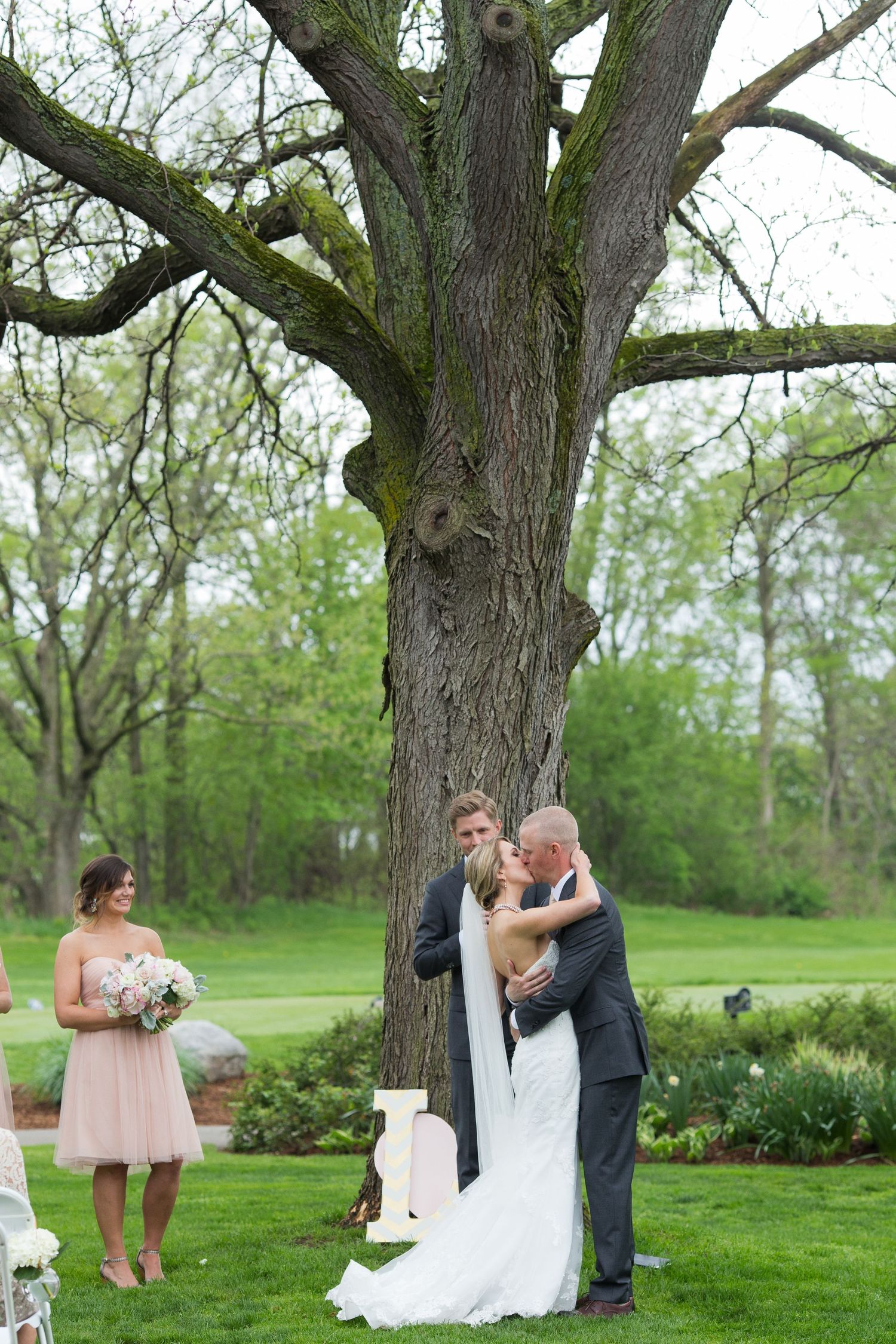 Wedding photo session in a lush green park with large trees creating a natural backdrop.