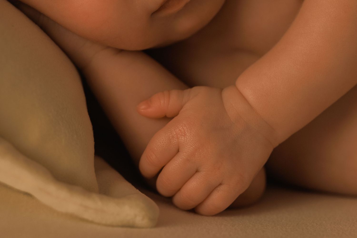 Close-up view of small baby feet and hands against a soft beige background.