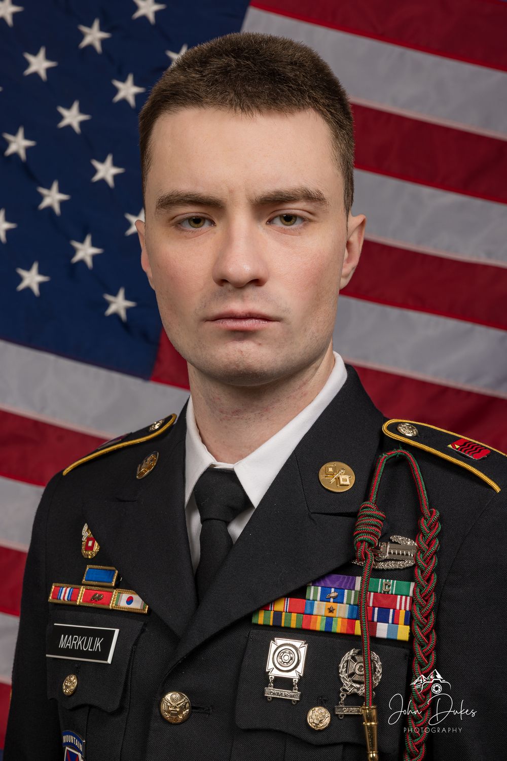 Military portrait of service member in dress uniform with medals against American flag background.