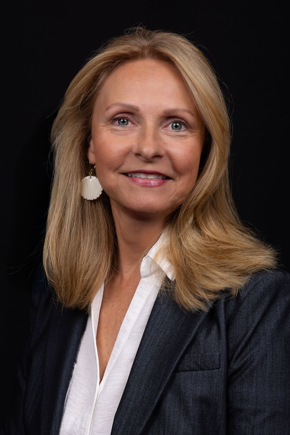Corporate headshot of person in dark suit jacket and white blouse against black background.