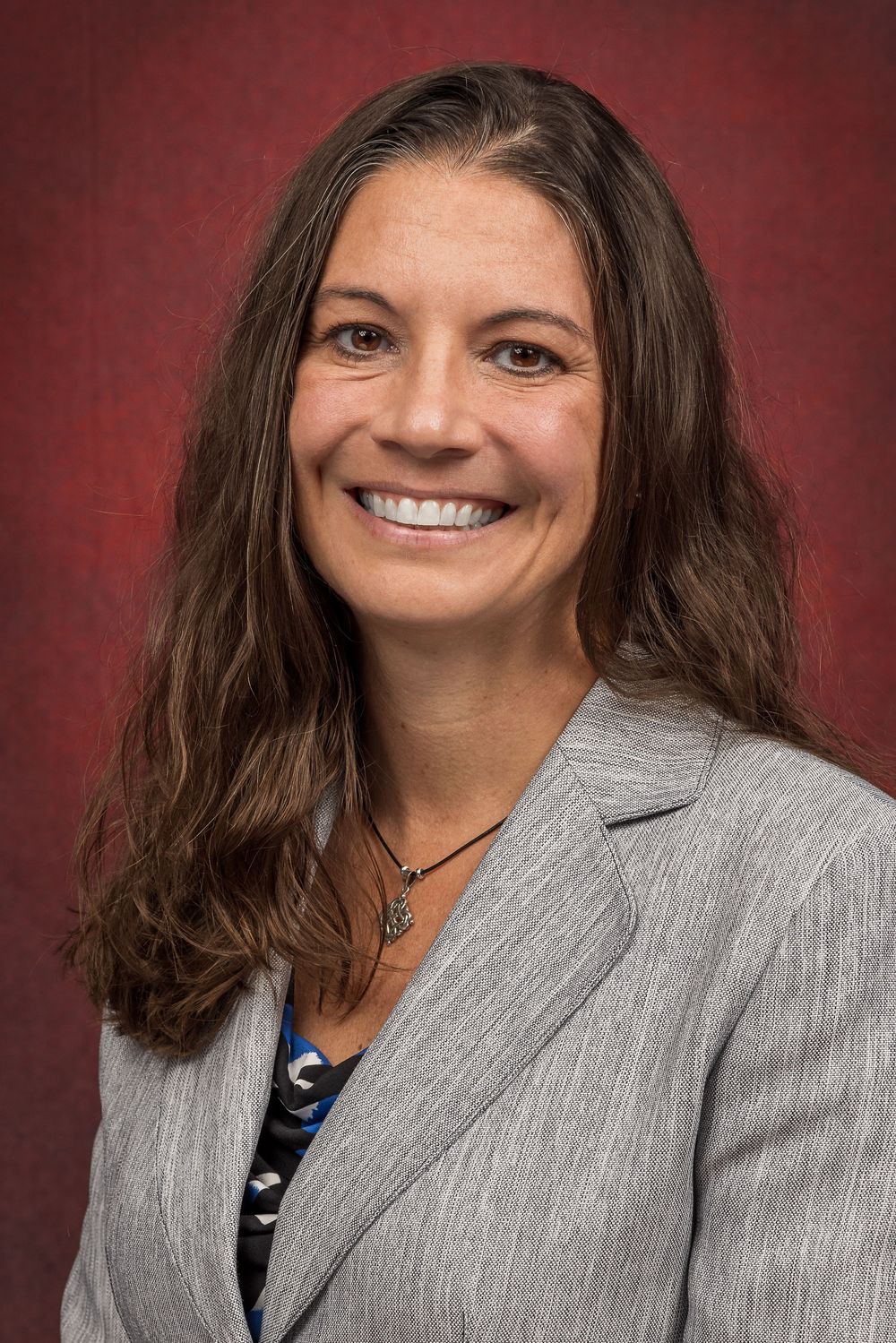 Business portrait showing person in gray blazer with dark hair against red background.