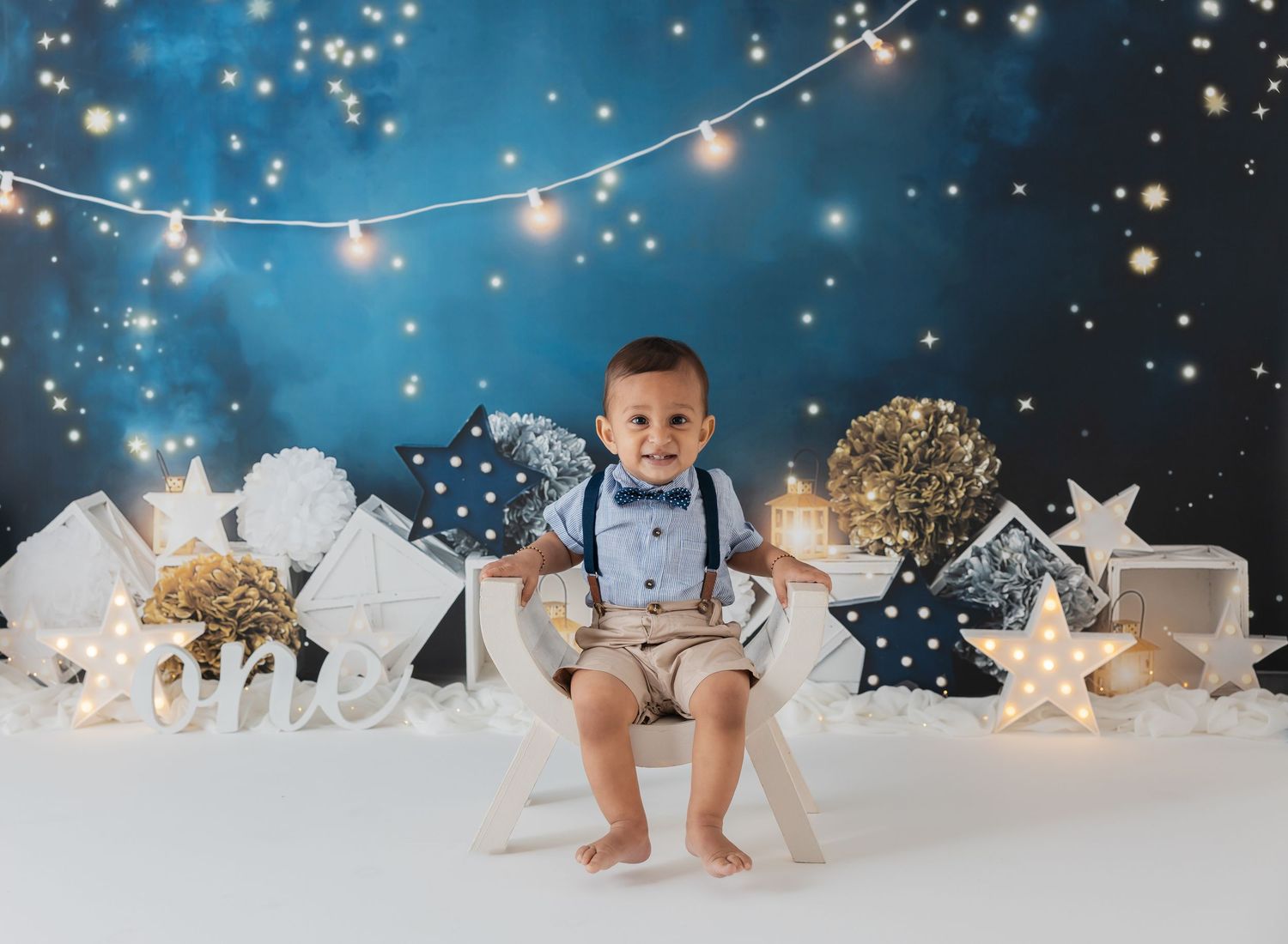 Festive winter cake smash setup with twinkling lights, stars and white decorations on a snowy backdrop.