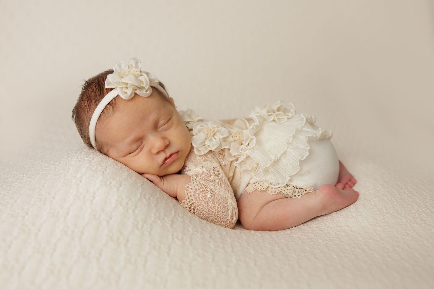 Peaceful newborn portrait in cream lace wrap on white backdrop.