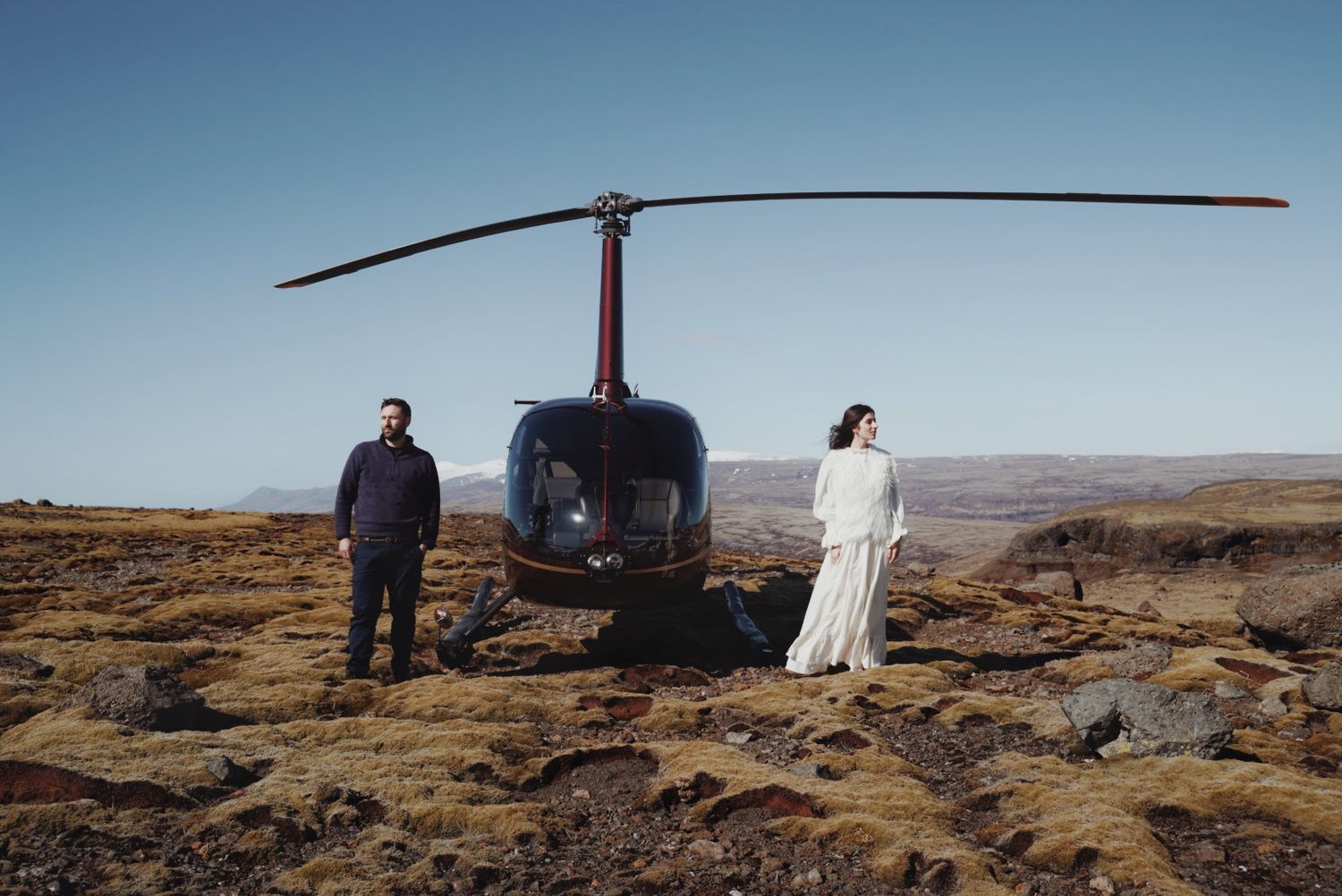 Couple standing beside a helicopter in the secluded mountains of Hvalfjörður, Iceland
