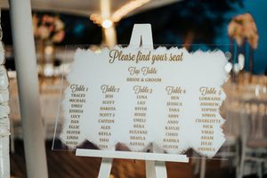 A wedding seating chart display with elegant white lettering on glass panels in a reception venue.