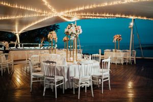 String lights create a warm ambiance across the ceiling of an elegant white wedding reception tent at dusk.