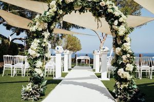 Elegant outdoor wedding ceremony setup with white floral arch and chairs overlooking the ocean.