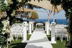 Elegant outdoor wedding ceremony setup with white chairs and floral arch overlooking the ocean on a sunny day.
