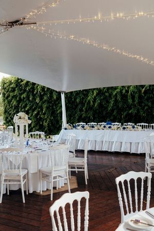 White chairs and tables set up under a tent canopy with string lights for an elegant outdoor wedding reception.
