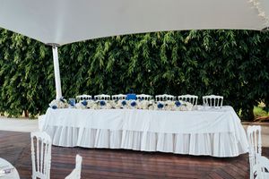 A long white banquet table decorated with blue and white floral arrangements extends down an outdoor venue.