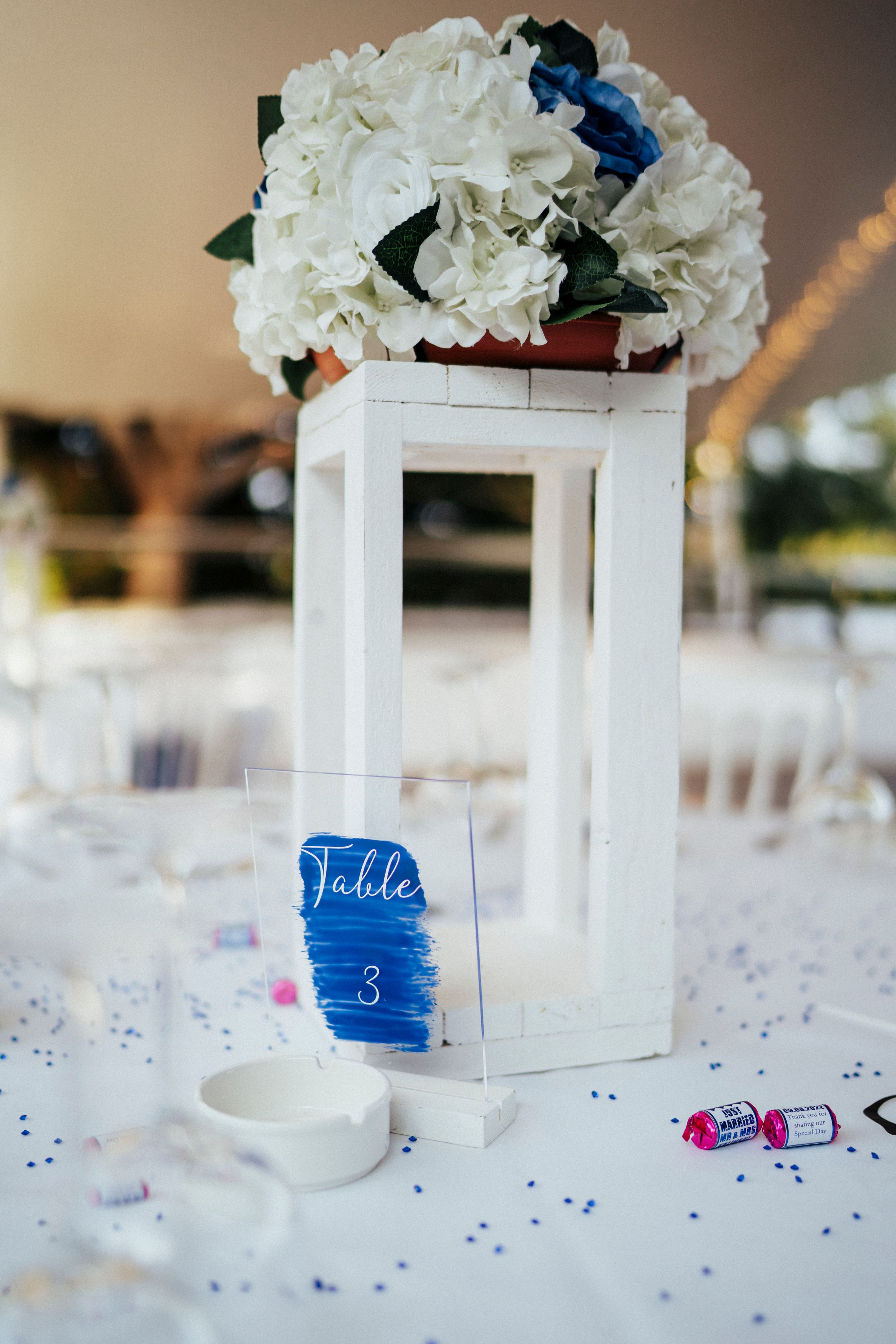 White decorative boxes with hydrangea flowers and blue accents arranged on a table with scattered confetti.