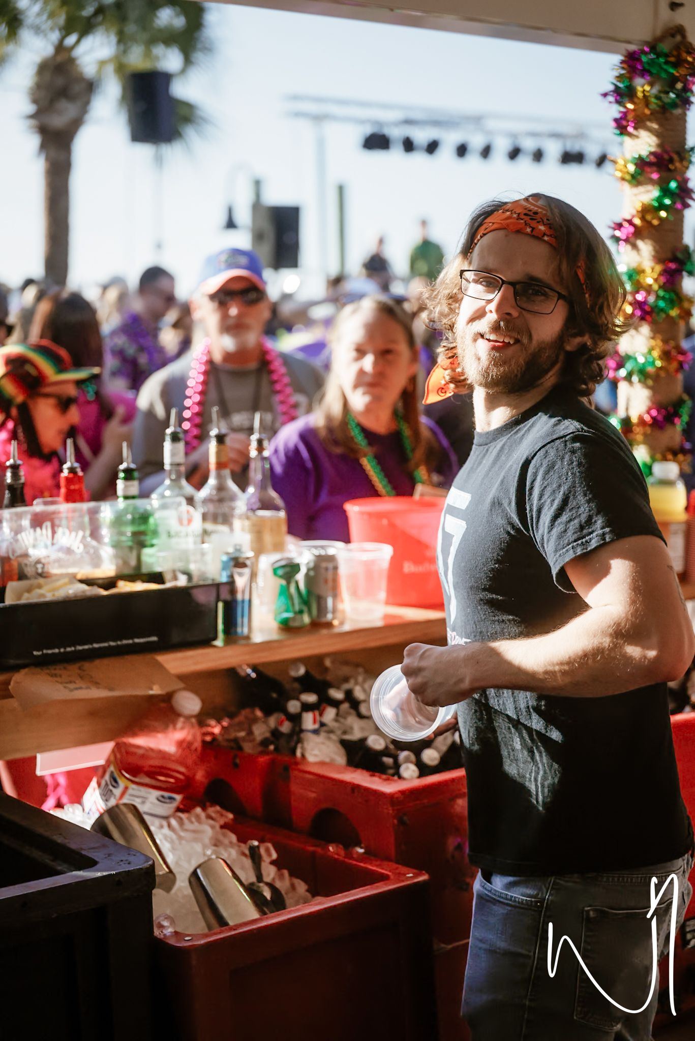 A bartender serves drinks at a festive outdoor bar decorated with Christmas lights and palm trees in the background.