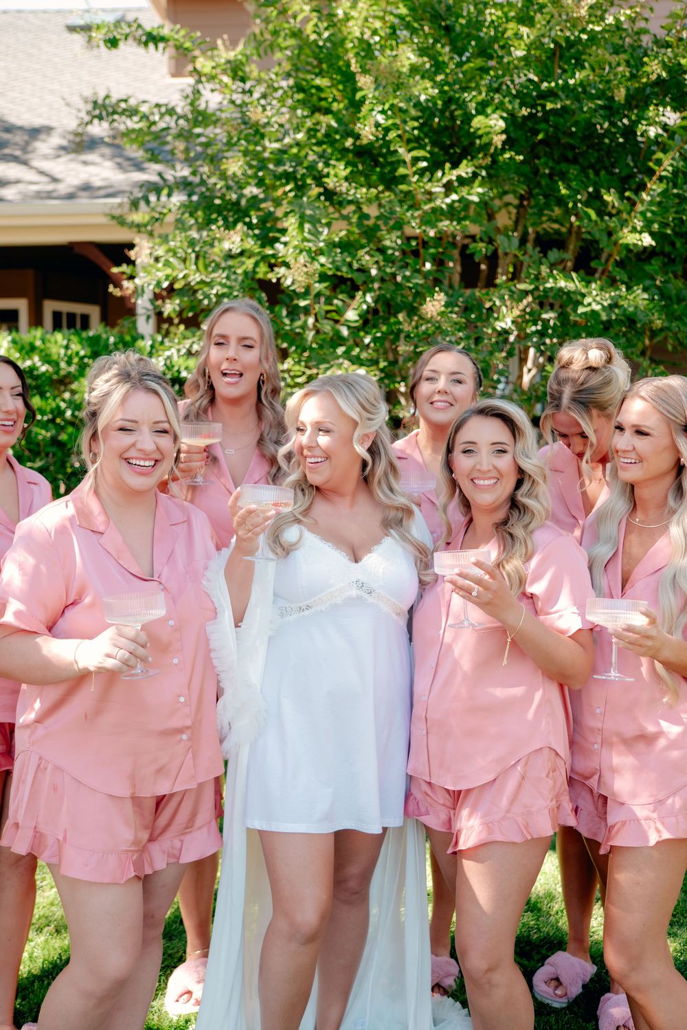 Group wearing matching pink and white loungewear posing together outdoors in front of greenery.
