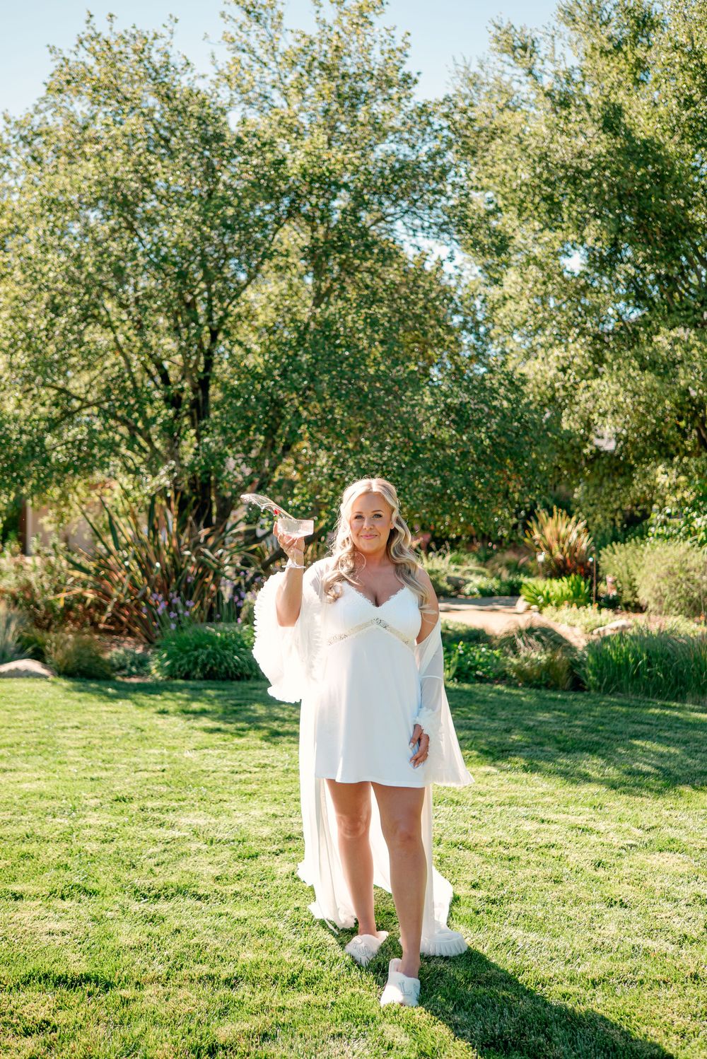 Playful sequence of a person in white dress twirling and dancing on a grassy lawn with trees in the background.