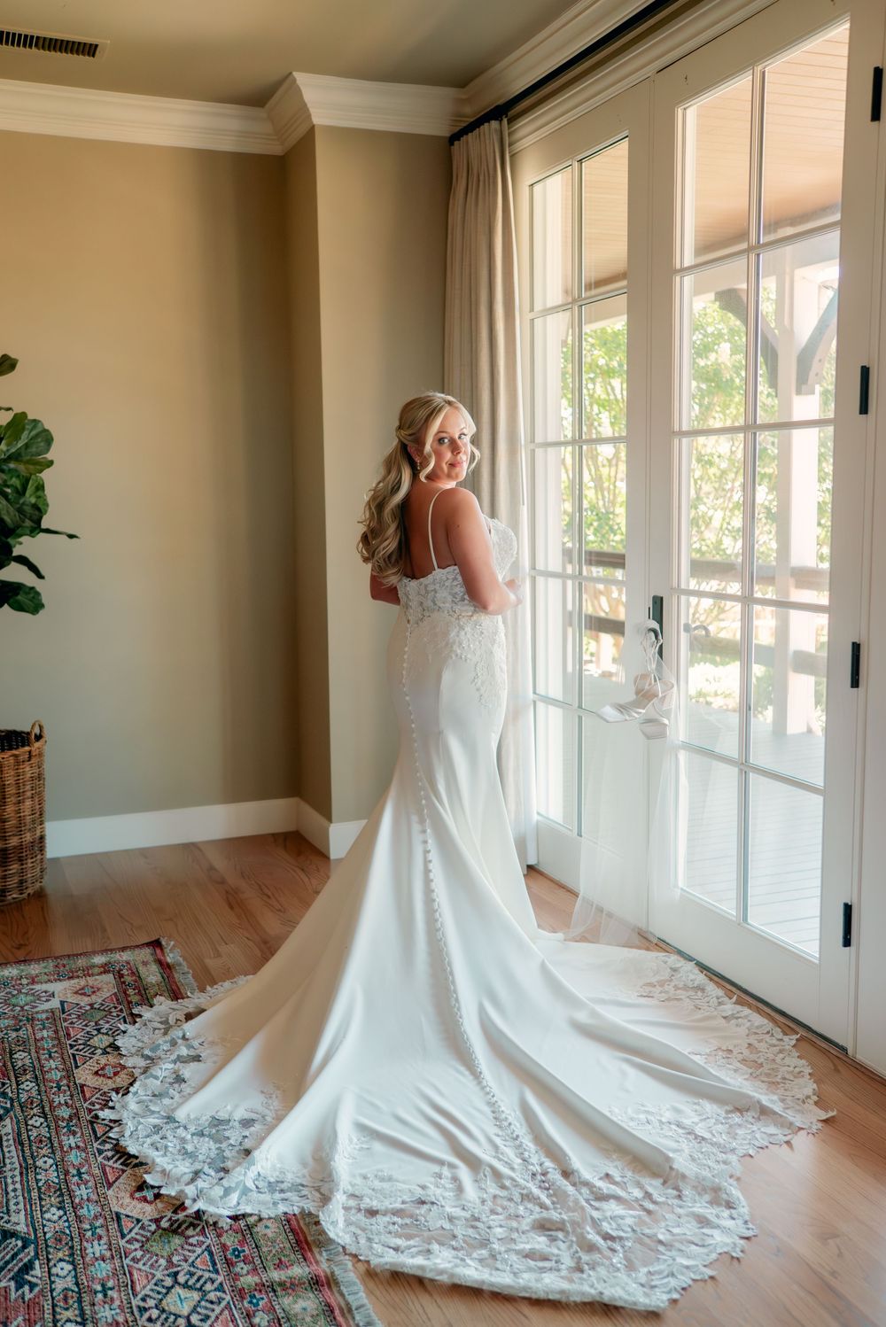 Elegant white wedding gown with lace train spreads beautifully across hardwood floor in bright room.