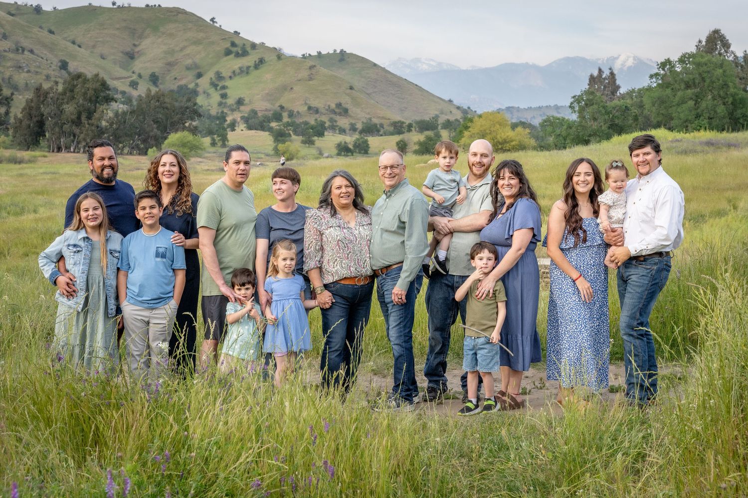 A group of people standing together in a grassy field with rolling hills and mountains in the background.
