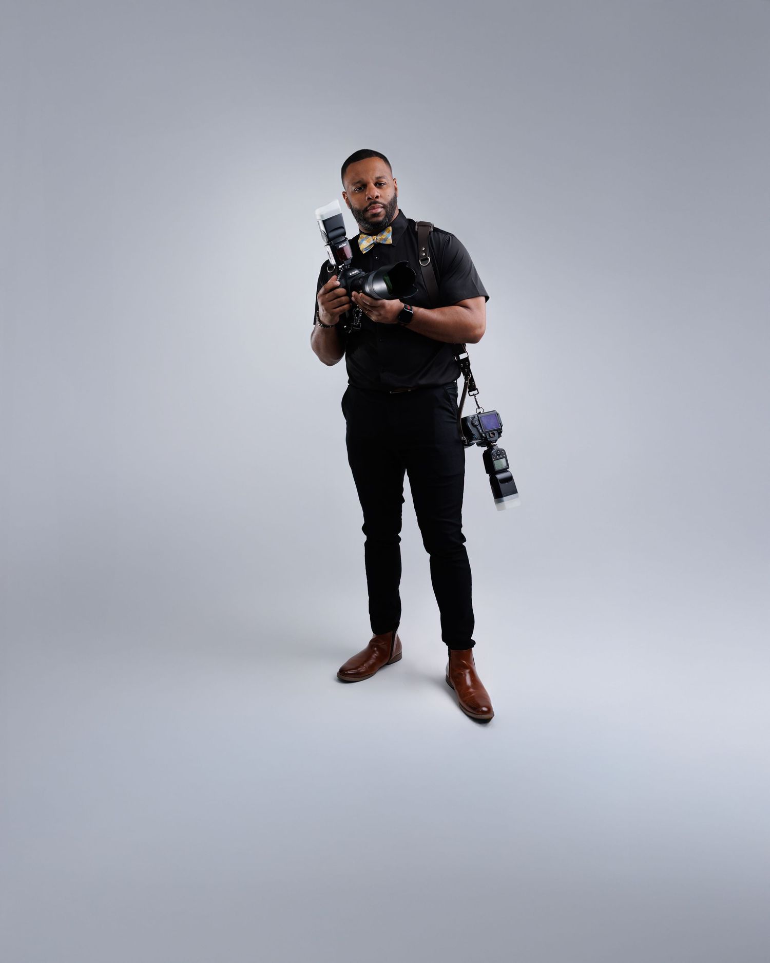 Professional photographer in black attire demonstrates dynamic shooting positions against gray studio background.