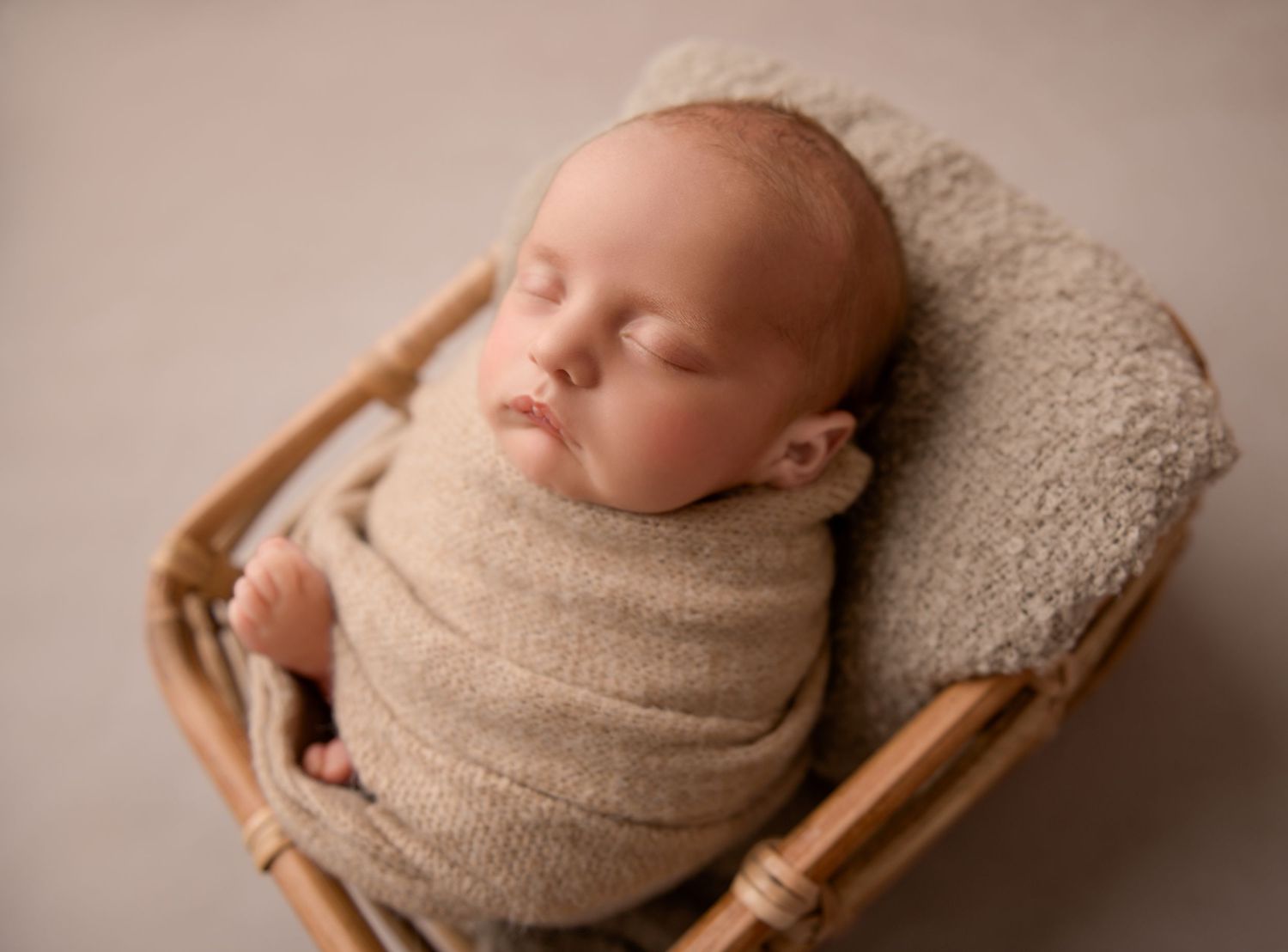 A collage of newborn photography poses showing a sleeping baby wrapped in a neutral knitted wrap on a wooden prop basket.