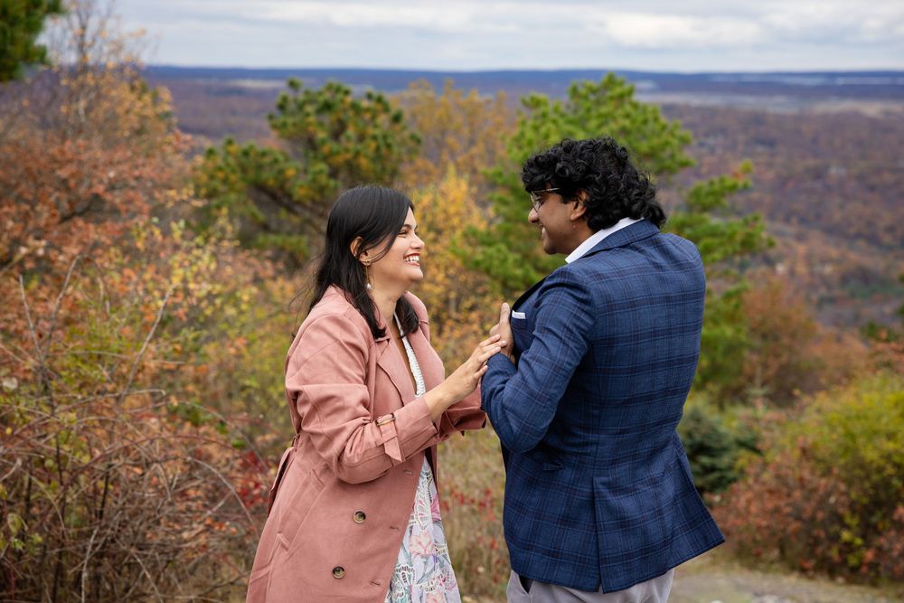 Couple sharing a romantic moment outdoors during fall foliage engagement proposal on a scenic overlook.